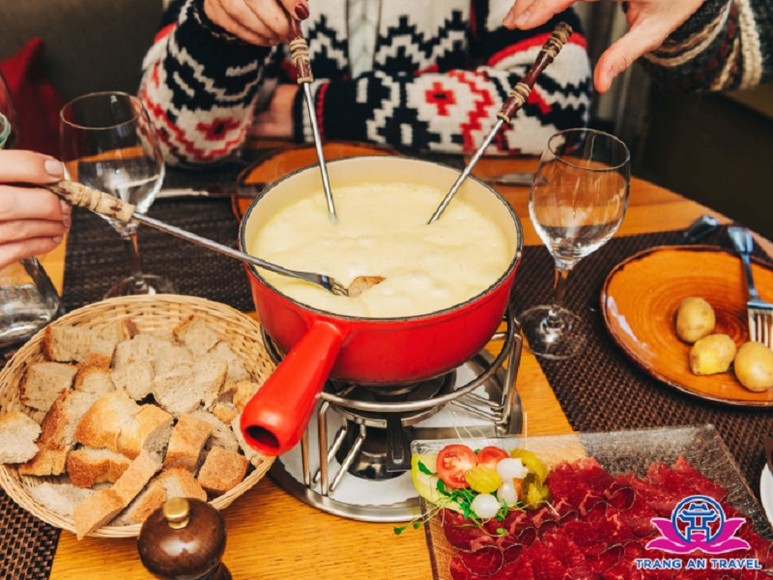 Khách du lịch cùng chấm bánh mì vào nồi fondue phô mai